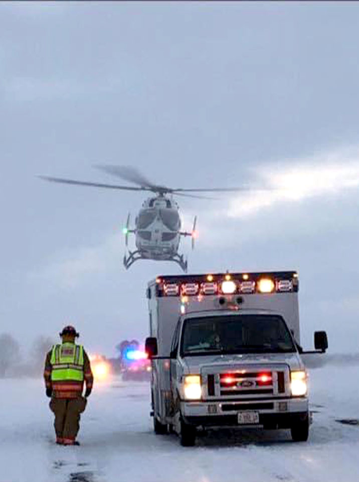 ambulance on snow covered roadway with life flight helicopter overhead